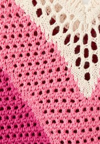 Tissu tricoté rose avec des motifs en zigzag alternant rose clair et rose foncé, partiellement recouvert de dentelle blanche au crochet avec des trous en forme de losange.