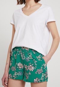T-shirt bianca in cotone a scollo a V abbinata a pantaloni corti verdi con stampa floreale, caratterizzati da una vita elastica e tasche laterali. Tessuto morbido, vestibilità casual.