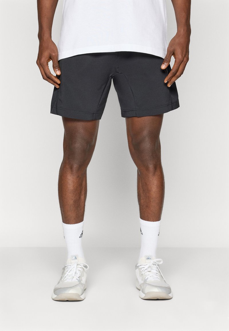 Zwarte sportshorts met een getailleerde pasvorm, platte naden en een lengte tot het midden van de dijen, gecombineerd met witte crew sokken en lichtgekleurde sneakers.