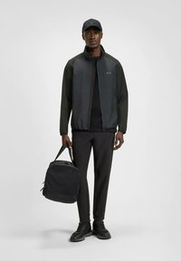 Juoda sportinė striukė su užtrauktuku, juoda marškinėliai ir kelnės, derinami su juoda rankine ir batais. Lygi tekstūra, modernus kirpimas, minimalistinis dizainas.