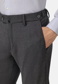 Grå skräddarsydda byxor med en strukturerad yta, featuring en slät front, sidofickor och knappdetaljer på midjan.