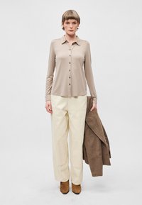 Bežna košulja dugih rukava sa gumbima, krema široke hlače, smeđi kaput prebačen preko ruke i smeđe čizme do gležnja. Jednostavna, glatka tekstura.