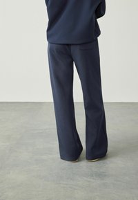 Marinblå, vida byxor gjorda av mjukt material med en slät textur och en bakfickadetalj. Lämpliga för avslappnat eller ledigt bruk.