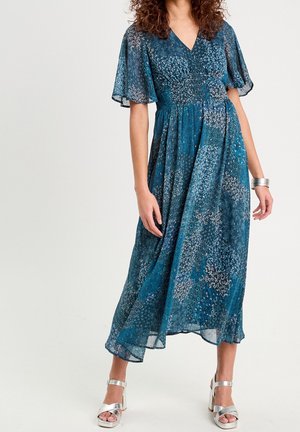 Une robe maxi florale bleu sarcelle avec des manches courtes volantées et un col en V. Fabriquée en matériau léger, elle présente une taille cintrée et une jupe fluide.