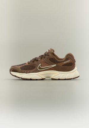 Zapatilla de running Nike marrón con paneles de malla y suela blanca, vista de lado sobre un fondo neutro.
