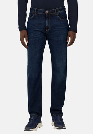 Jeans blu scuro con taglio dritto, cuciture a contrasto, design a cinque tasche e chiusura con bottone metallico, abbinati a sneaker blu navy.