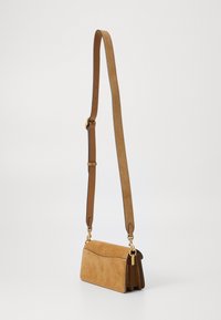 Džinsasta crossbody torba iz svetlo rjave kože s glatkim kožnim remenom, koja ima zlatne detalje i suptilne zakrivljene šavove.