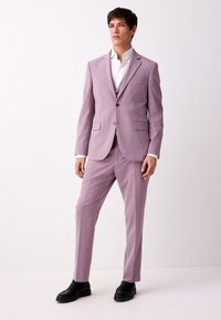 Abito color viola chiaro con vestibilità slim, caratterizzato da rever a lancia, due bottoni e pantaloni coordinati. Indossato con camicia bianca e scarpe nere.