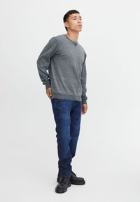 Gråstrikket genser med rund hals, kombinert med mørkeblå jeans med en lett tekstur og sorte snørebåndsstøvler.