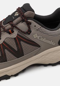 Chaussure de randonnée Columbia avec une tige en maille grise et des accents orange, semelle en caoutchouc texturée, et lacets noirs pour un maintien sécurisé et une flexibilité.
