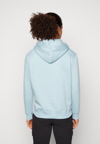 Felpa con cappuccio azzurro chiaro, con polsini e orlo a costine. Presenta una texture liscia e una vestibilità comoda. Indossata con pantaloni cargo neri.