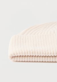 Folded cream-colored ribbed knit beanie hat on a white surface.