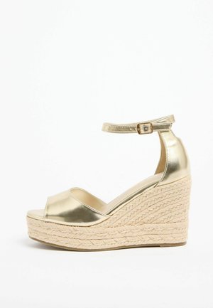 Sandalia de cuña metálica dorada con correa en el tobillo y hebilla, con suela de plataforma de cuerda tejida.