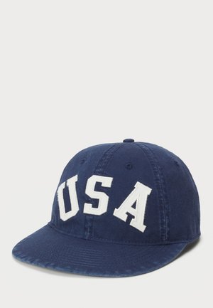 Casquette bleu marine en coton, avec des grandes lettres blanches brodées "USA" sur le devant. Conçue avec une visière courbée et une sangle ajustable.