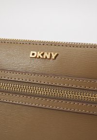 Aukso atspalvio dirbtinės odos piniginė su auksiniu "DKNY" logotipu ir tvirtu užtrauktuku. Textūruota paviršius su matomomis siuvimo detalėmis.