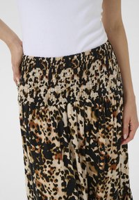Leopard print skirt featuring a smocked waistband, elastic texture, and flowing fabric in beige, black, and shades of brown.