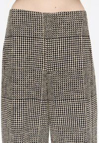 Czarno-kremowe spodnie w kratkę wykonane z teksturowanej tkaniny o wyraźnym wzorze kratki i wysokim stanie.