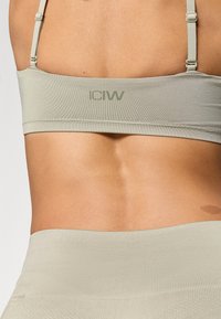 Ανοιχτό πράσινο αθλητικό σουτιέν με λεπτές ρυθμιζόμενες τιράντες, λείο υλικό και λογότυπο τυπωμένο στην πλάτη, συνδυασμένο με ψηλόμεσα κολάν.