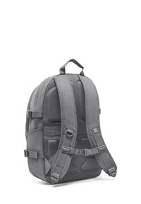 Rucsac din țesătură gri, cu bretele moi, detalii din plasă, bretele laterale ajustabile și mânere superioare pentru transport.