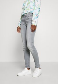 Jeans skinny grigi fatti di denim, con un classico design a cinque tasche. Abbinati a sneaker bianche e una camicia a maniche lunghe floreale.