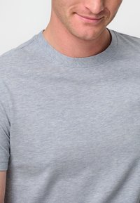 Ljust grå t-shirt med kort ärm och rund halsringning. Materialet verkar mjukt med en subtil textur och en avslappnad passform. Inga framträdande mönster eller detaljer.