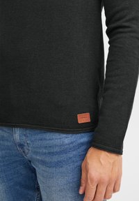 Svart langermet teksturert skjorte med en brun lærmerkelapp som har "BLEND" nederst på sømmen, paret med blå denim jeans.