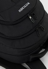 Mochila negra hecha de tela texturizada con tres compartimentos con cremallera y correas de malla ajustables. Presenta un logo blanco y herrajes de cremallera negros.