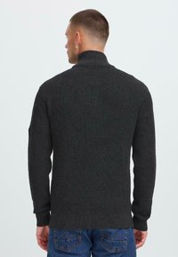 Uomo di spalle che indossa un maglione a coste grigio scuro con colletto alto e jeans blu.