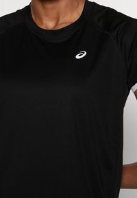 Czarna sportowa koszulka z krótkim rękawem, wykonana z gładkiego materiału. Z białym logo po lewej stronie i okrągłym dekoltem.