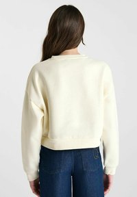 Crème-kleurige cropped sweatshirt met een zachte textuur en geribbelde zoom, gecombineerd met donkerblauwe jeans met hoge taille en stiksels op de achterzakken.