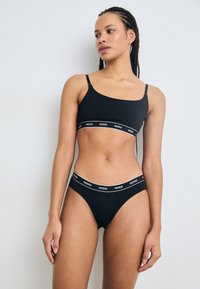 Set de sutien negru și bikini asortat, realizat din material moale, având benzi elastice cu logo-ul "HUGO" în alb. Bretele reglabile pe partea de sus.