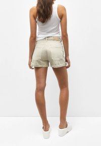 Shorts en jean beige clair avec des ourlets effilochés, deux poches arrière et une étiquette couleur tan sur la ceinture, assortis d'un débardeur blanc et de chaussures à plateforme.