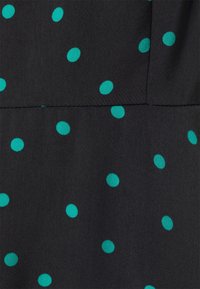 Tissu noir à texture lisse, présentant un motif de pois bleu sarcelle répartis uniformément sur toute la surface.