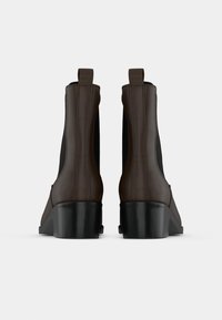 Καφέ δερμάτινες μπότες γύρω από τον αστράγαλο με ελαστικές πλευρικές πλάκες και χαμηλές γόβες, με λεία υφή και μινιμαλιστικό σχέδιο.