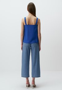 Blauw mouwloos topje met brede banden, gecombineerd met lichtblauwe wijde jeans en witte hoge hakken sandalen. Soepele stof, minimalistisch ontwerp.