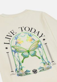 Beige katoenen t-shirt met een grote, kleurrijke vlinderafbeelding omgeven door bloemenontwerpen en de tekst "LEEF VANDAAG" in dikke zwarte letters.