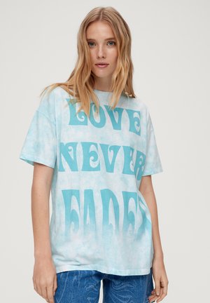 T-shirt tie-dye bleu clair avec un texte turquoise en gras affichant "L'AMOUR N'A JAMAIS FANNÉ." Fabriqué en coton doux, avec des manches courtes et une coupe décontractée.