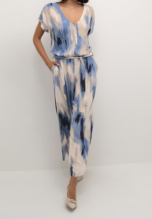 Sinivalkoinen kuviollinen haalariasu, jossa on V-aukko, lyhyet hihat, vyö ja taskut. Kevyt kangas ja levenevä malli.