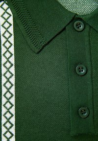 Rohelisest soonikust polo-särk, millel on kolm nuppu ja valge vertikaalne triip, millel on mööda ühte külge roheline teemantmuster.