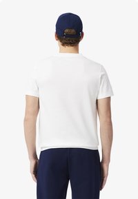 Camiseta de algodón blanca de manga corta, combinada con pantalones azul marino. La vista desde atrás muestra un diseño simple y una textura suave, sin patrones distintivos.