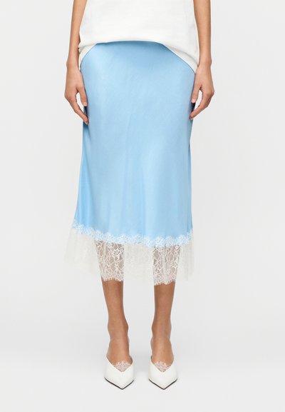 Jupe midi en satin bleu clair avec bordure en dentelle blanche à l'ourlet. Présente une texture lisse et une silhouette ajustée. Portée avec des chaussures blanches à bout pointu.