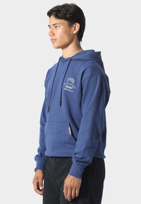 Felpa blu con cappuccio regolabile, tasca a canguro frontale, dettagli ricamati e polsini a costine. Realizzata in tessuto morbido e confortevole.