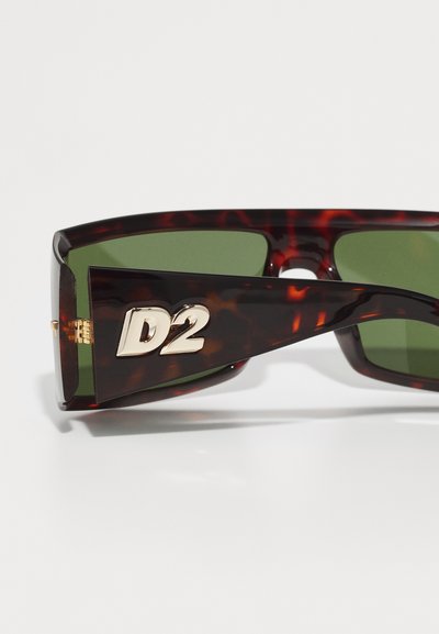 Ochelari de soare din material țestoasă, cu lentile verzi, având un logo auriu îndrăzneț "D2" pe laterale. Textură netedă, formă rectangulară și mânere groase.