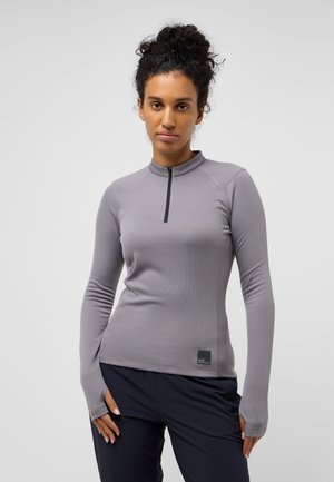 Maglietta atletica a maniche lunghe di colore grigio chiaro con colletto alto e zip a quarto. Presenta aperture per i pollici nei polsini e un'etichetta logo laterale.