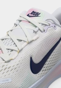 Chaussure de course Nike blanche avec des accents roses et bleus, des lacets blancs et une étiquette "RUN" sur la languette.