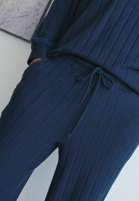 Marineblaues, geripptes Lounge-Set mit lockerer Passform. Verfügt über einen Kordelzugbund und Taschen. Weiche Textur und dezente vertikale Streifen.