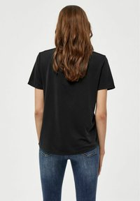 Schwarzes kurzärmliges T-Shirt mit entspannter Passform. Glatte Textur und abgerundeter Saum, getragen mit blauen Denim-Jeans.