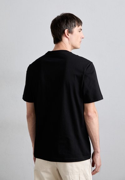T-shirt en coton noir avec un col ras du cou, des manches courtes et une coupe décontractée, présentant une texture lisse et un design minimal.
