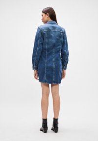 Τζιν φόρεμα με ελαφρώς ξεθωριασμένο μπλε χρώμα, μακριά μανίκια, κλείσιμο με κουμπιά και επενδεδυμένη ραφή στην πλάτη. Φορτωμένο με μαύρες μποτάκια μέχρι τον αστράγαλο.