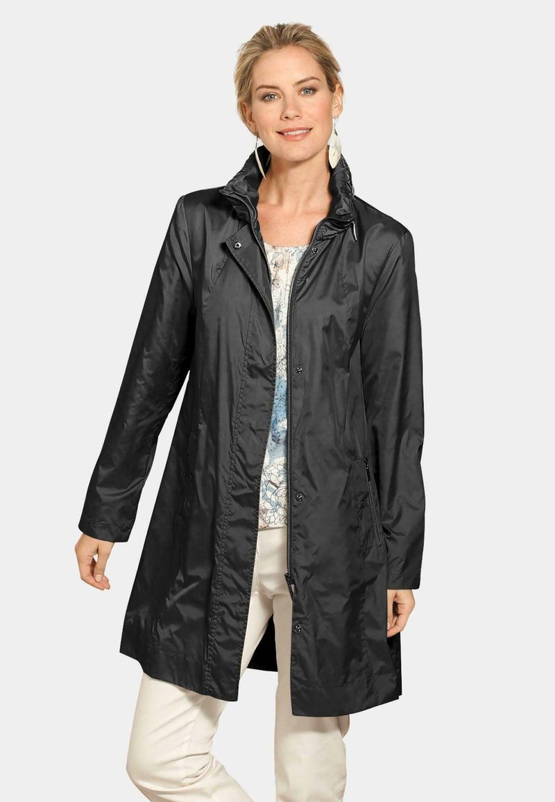 Zwarte regenjas met een hoge kraag, drukknoopsluitingen en zijzakken. Gemaakt van een lichtgewicht, glanzend materiaal voor bescherming tegen het weer.